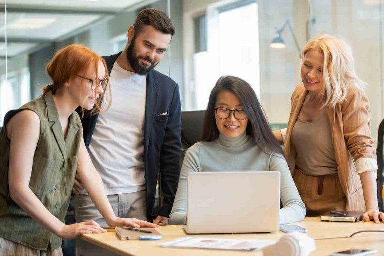 Pretty Asian businesswoman looking at laptop display among her happy colleagues