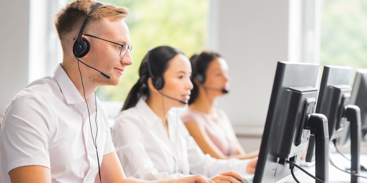 a group of people wearing headsets and looking at computers representing a hero image for blog about hospitality outsourcing