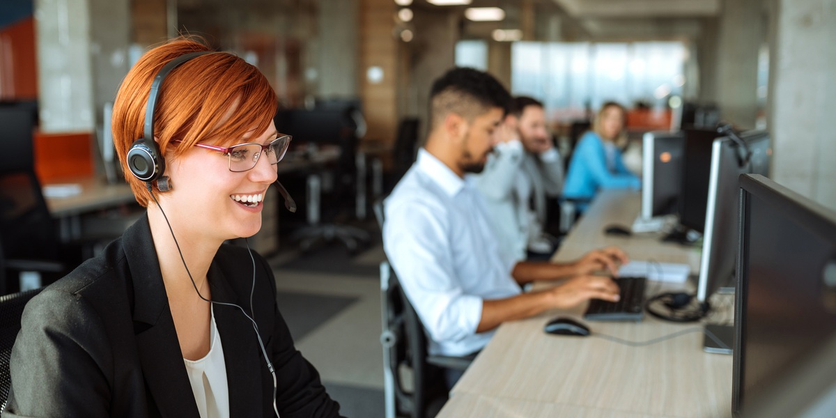 a woman wearing a headset and sitting at a desk with other people in the background representing the hero image for the blog post about ecommerce outsourcing