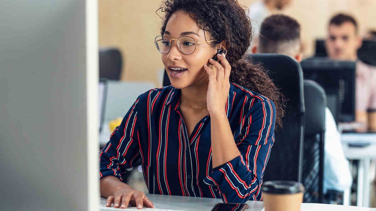 young business woman working with laptop while talking with earphone sitting in a coworking place.