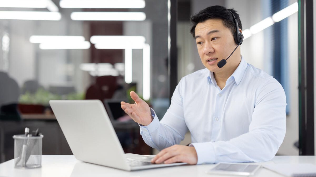 A business professional engages in a discussion during a video call in a well-lit contemporary office setting.